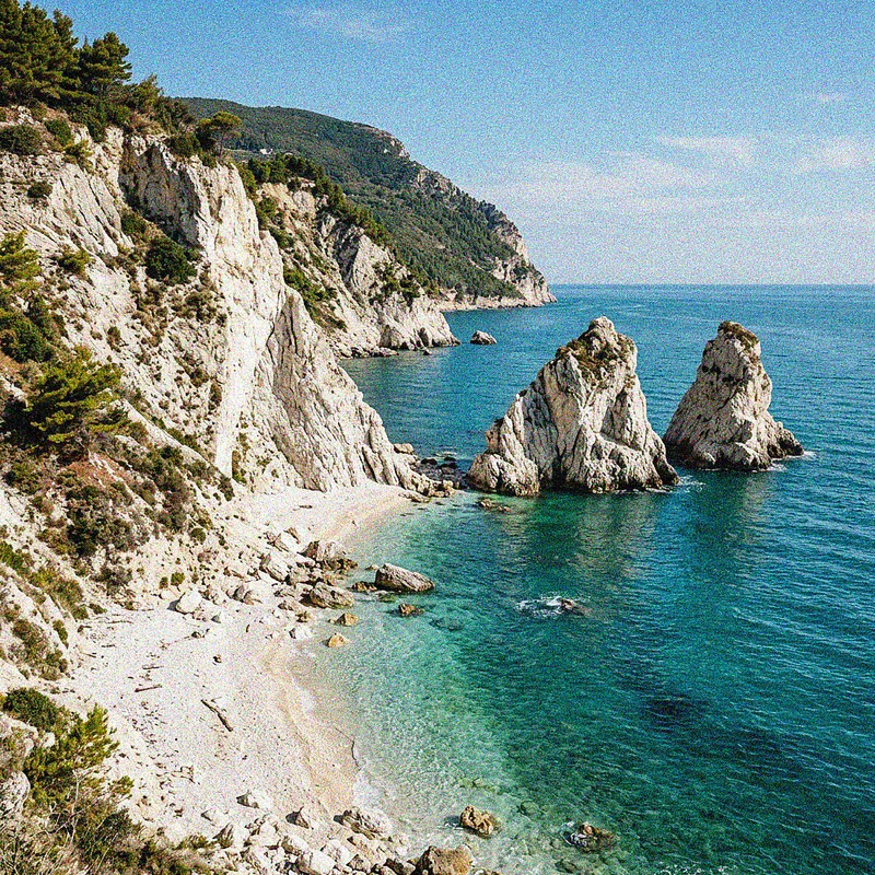 La spiaggia delle Due Sorelle a Sirolo con drammatiche scogliere bianche e acqua turchese.
