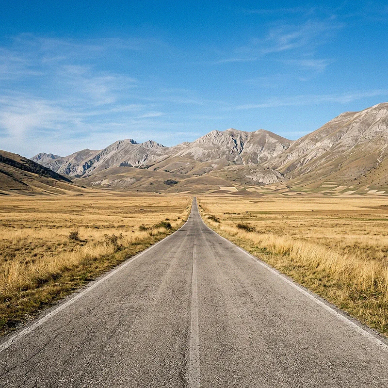 Una strada asfaltata e solitaria attraversa i campi dorati di Castelluccio di Norcia